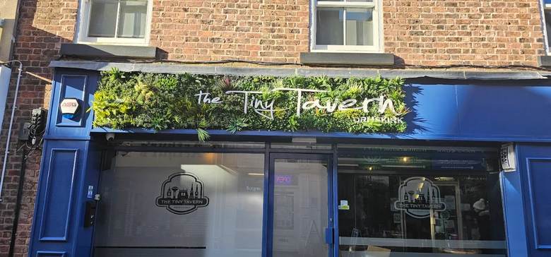 Close-up of the Tiny Tavern sign above the front door, with a living green wall
